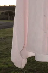 Camisa oversize color rosa claro a rayas verticales blancas, con cuello mao y mangas largas con puños elásticos.