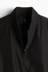 Campera bomber negra liviana con cuello elevado acanalado y cierre delantero. Tiene bolsillos laterales y un bolsillo interior, todos con cierre. Los puños y el bajo son acanalados.