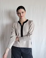 Remera color beige con cuello redondo y ribete negro, mangas largas con frunce en los hombros y corte recto.