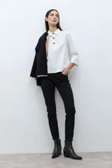 Blusa blanca con estampado de pequeños lunares negros, cuello camisero y botones frontales oscuros. Mangas tres cuartos con ligero vuelo en el puño.