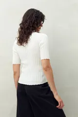 Top de manga corta color blanco, tejido con textura acanalada, cuello alto y terminaciones onduladas en mangas y ruedo.