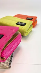 Billetera corta de tela capitoneada, con cierre alrededor y tapa. Incluye varias reparticiones con tarjeteros y bolsillos internos. Correa de mano desmontable.