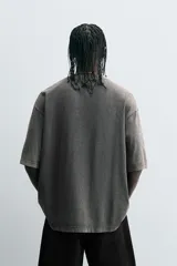 Camiseta gris con efecto lavado, cuello redondo y manga corta. Estampado frontal con conejo, texto y efecto de pintura.