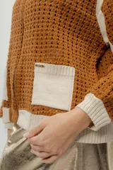 Chaqueta estilo bomber tejida color marrón con detalles en beige, cierre frontal y bolsillos delanteros.