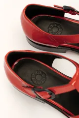 Sandalia roja de cuero vacuno con diseño de tiras entrecruzadas y hebilla lateral. Tiene suela de cuero artesanal y taco bajo.