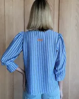 Blusa color beige con cuello con volados, mangas largas abullonadas con puños elásticos y cierre con botones en la parte delantera.