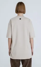 Remera de corte crop y calce oversize, con hombros caídos, confeccionada en algodón premium americano color beige claro. Posee cuello redondo rib al tono y doble costura.
