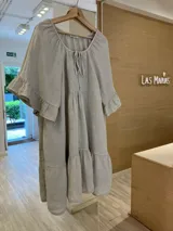 Vestido de lino color beige, con escote con lazo, mangas cortas amplias con volados y volados en el ruedo.