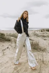 Pantalón plateado de cuero sintético con tirantes desmontables y corte ancho.