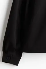 Campera negra de corte recto, con cuello camisero, cierre frontal con cremallera metálica, bolsillos laterales ribeteados y puños abotonados. Forrada.