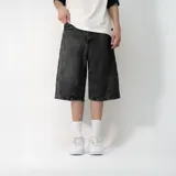 Bermuda de denim negro lavado, corte ancho y largo (tipo culotte o bermuda ancha), con paneles frontales definidos por costuras verticales.