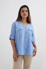 Camisa celeste de algodón con escote en V, mangas 3/4 con trabilla y dos bolsillos con solapa abotonada en el pecho.