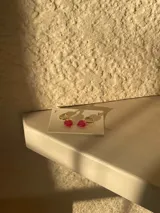 Par de aros colgantes con argolla dorada y dije de corazón de vidrio rojo.