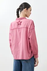 Camisa fucsia de manga larga con cuello camisero y cierre frontal con botones. Presenta apliques de estrellas bordadas en el frente y en el cuello.