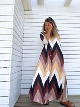 Vestido camisero largo con estampado chevron en tonos chocolate, beige, negro y crudo. Tiene cuello camisero, mangas largas y cierre frontal con botones. Presenta aberturas laterales en el ruedo.