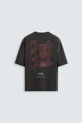 Camiseta negra de corte holgado con cuello redondo y mangas cortas. Estampado frontal con una ilustración de una mujer en un cohete y la leyenda "Cherry Pilot Blush Delight".