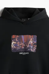 Canguro negro con capucha y bolsillo tipo canguro. Estampa rectangular en el pecho con imagen de banda musical en vivo y texto "Unplugged".