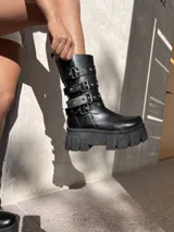 Bota negra de ecocuero con caña media, plataforma track y tres correas con hebillas plateadas.