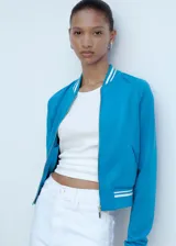 Chaqueta deportiva azul con cierre frontal, cuello redondo y terminaciones con rayas blancas en cuello, puños y ruedo.