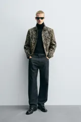 Cazadora corta (cropped fit) de piel con acabado de pelo, estampado abstracto en tonos negro y beige/tostado. Presenta cuello solapa, manga larga y cierre frontal con botones metálicos.