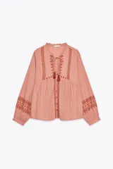 Blusa color rosa pálido de algodón con cuello redondo con volantes y cordón. Escote pico y manga larga. Detalle de bordados combinados a contraste color marrón. Cierre frontal con botones.