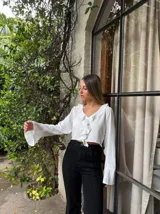 Blusa blanca crop con escote en V y volados, mangas largas acampanadas.