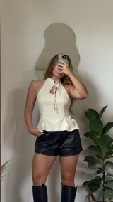 Top color manteca, ajustado al cuerpo, con escote halter y detalle de lazo en el centro del busto. Presenta un peplum sutil en la parte inferior.