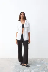 Camisa blanca de lino con cuello clásico, cierre frontal con botones, mangas largas con puños abotonados y dos bolsillos de parche en el pecho.