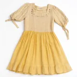 Vestido de dos tonos, con corpiño color beige claro y falda amarilla. El corpiño tiene escote cuadrado y bordado floral en tonos rojizos y beige. Las mangas son cortas y abullonadas, ajustadas con lazos. La falda es fruncida y termina con un ruedo con volado.