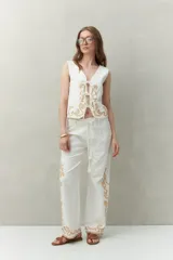 Chaleco blanco de algodón con bordados de cadenas doradas y lazos frontales.