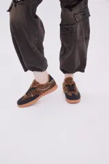 Zapatillas bajas de cuero sintético con estampado animal print, puntera y cordones negros, suela color caramelo y detalle en el talón color blanco.