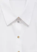Camisa blanca de popelina de algodón, corte crop, con cuello camisero, manga larga con puños abotonados, bolsillo de parche en el pecho y cierre frontal con botones.