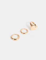 Set de tres anillos dorados de metal con diferentes diseños: uno liso, uno con forma de corazón y uno con forma de domo.