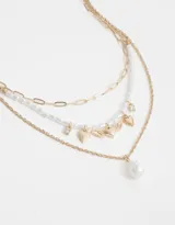 Set de tres collares cortos dorados. Uno con eslabones, otro con perlas y el tercero con dije de corazón alado y perla colgante.