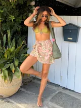 Falda pareo corta, color rosa pálido con estampado en tonos ocre/dorado. Presenta un diseño envolvente que se ajusta con un lazo lateral.