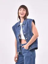 Chaleco de denim azul medio, con cuello camisero, cierre frontal de botones y bolsillos delanteros. Diseño sin mangas con hombros marcados.