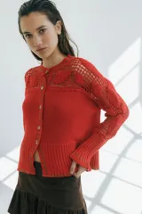 Cárdigan rojo de algodón acanalado con calce entallado, mangas largas con volados y detalles de crochet hechos a mano en hombros y mangas. Presenta vivos de color en cuello, puños y frente, y cierre frontal con botones. 