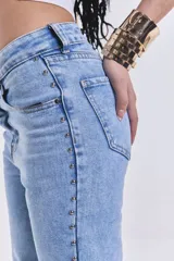 Jean de denim celeste, de corte recto y tiro medio, sin lycra. Presenta tachas metálicas en los laterales.