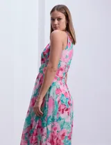 Vestido largo de gasa estampada con flores rosas y turquesas sobre fondo blanco. Tiene escote halter con ojal, cintura fruncida y falda con sobrecapa.