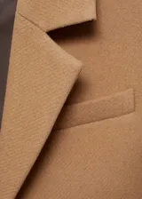 Abrigo largo color beige con cuello de solapa, cierre de doble botonadura, mangas largas con puños abotonados, un bolsillo de ribete en el pecho y dos bolsillos de solapa en la parte frontal.