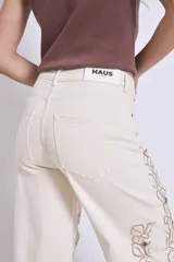 Pantalón de jean color crudo con bordados florales y aberturas en las piernas.