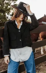 Chaqueta corta negra de cuero ovino con cuello camisero, cierre con botones, bolsillos plaqué y forro de algodón.