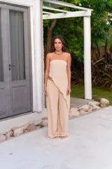 Conjunto de dos piezas color beige claro, compuesto por un top strapless con bajo asimétrico y un pantalón ancho de tiro alto.