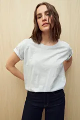 Remera de manga corta color gris claro, confeccionada en algodón con textura liviana y suave al tacto. Presenta costuras decorativas en los laterales y mangas con pequeño doblez.