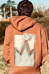 Canguro marrón con capucha y estampado en la espalda con diseño geométrico en tonos blanco, gris y naranja.