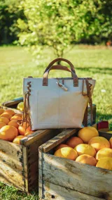 Cartera tipo tote de cuero color blanco con manchas doradas, doble asa corta y flecos de cuero en los laterales.