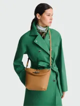 Bolso tipo bucket color marrón claro, con correa larga al hombro y cierre metálico plateado.