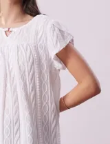 Blusa blanca labrada con cuello a la base, escote en V y aplique metálico. Tiene mangas cortas superpuestas.