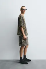 Sudadera relaxed fit con estampado de hojas en tonos verde, marrón y negro. Tiene cuello redondo, manga corta y bajo irregular con aberturas laterales.