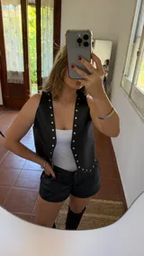 Chaleco negro de ecocuero con cuello en V y tachas plateadas.